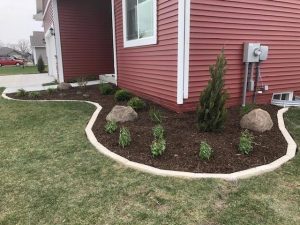 Mulch Garden surrounded by limestone edgers on corner of a red house by Norwalk Seasonal - Des Moines, Iowa