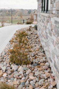 River Rock Landscaping along Sidewalk Norwalk Seasonal with a rock veneer on the house- Des Moines, Iowa