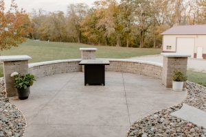 Concrete patio with stacked stone seating wall and a mobile firepit in the center