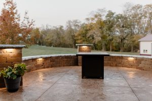 A poured and stamped concrete patio surrounded by a seating retaining wall showcasing the lights that are installed on retaining wall under the stone bench