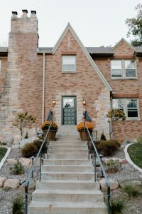 Walkway up to a Two Story brick house with a long staircase that has rock landscape elements along with plants on both sides.