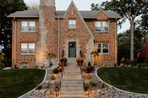 Photo of a 2 story brick house with a door in the middle that sits atoop a hill with a long staircase leading up to it. The staircase is landscaped on either side with a rock garden and shrubs. Also pictured are two porch pots. All landscaping done by Norwalk Seasonal Services