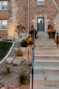 Close up on a rock garden next to a tall staircase leading up to the front door of a 2 story brick house.