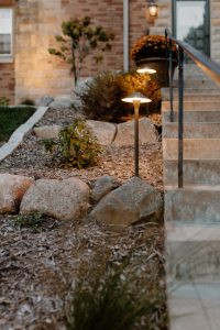 Closeup of two solar lights in a rock garden helping to light the stairway to a house at dusk.