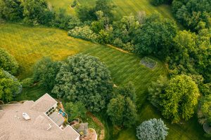 Aerial view of a mowed back lawn with trees, a house and garden