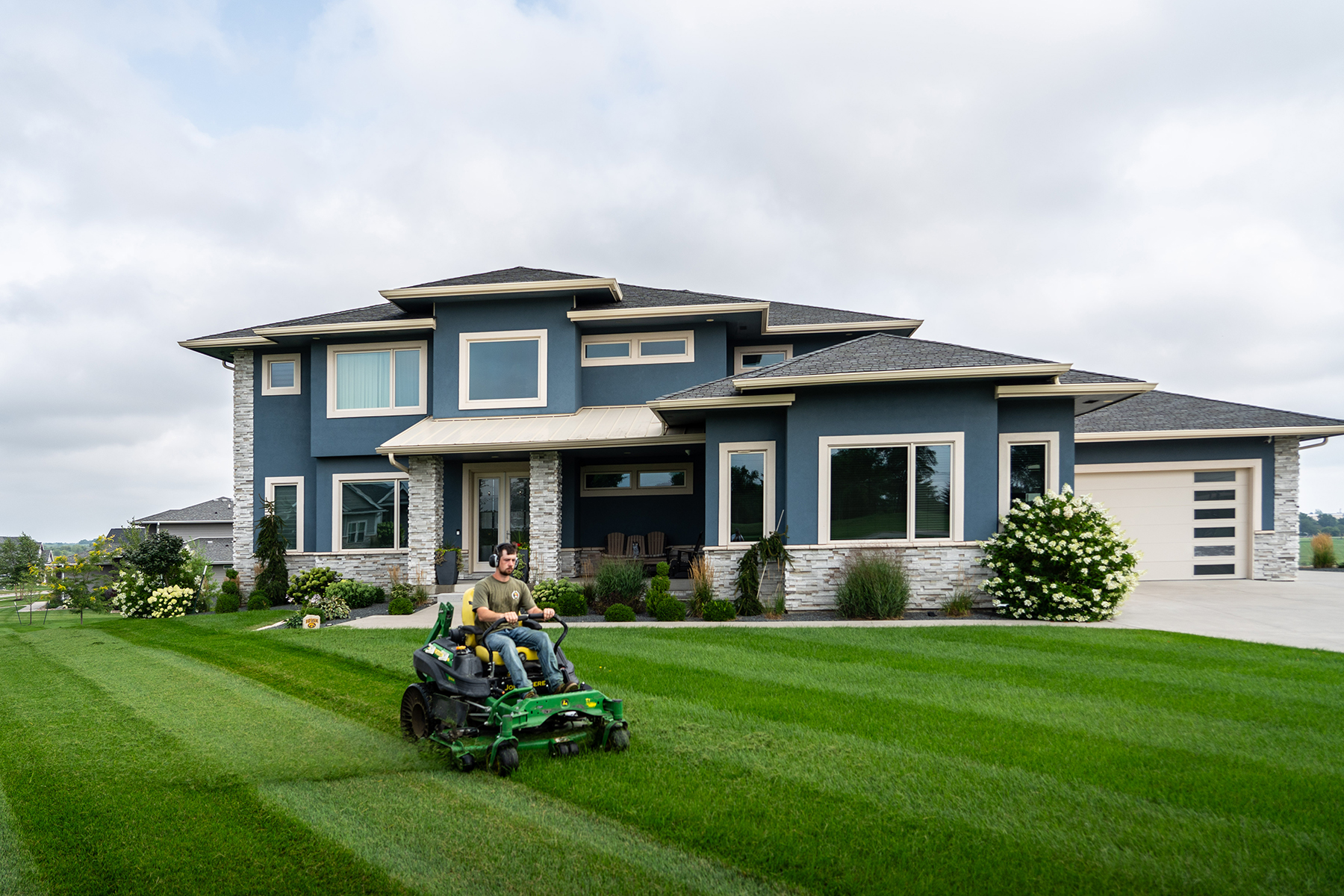 NSS Team mowing a large lawn in front of a blue two story house